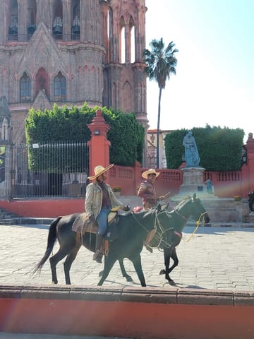 Cowboys riding past the pink towers of the Parroquia de San Miguel Arcángel