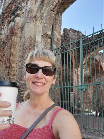 Stacy smiling with a coffee outside old stone church ruins